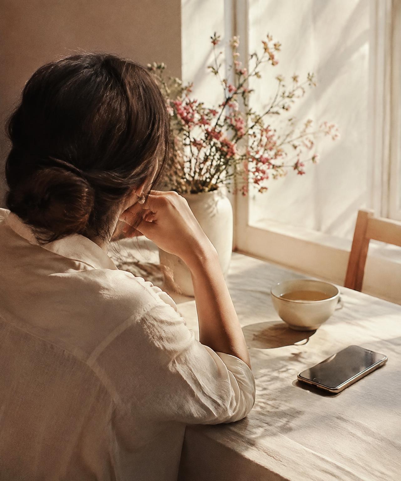 A calm woman by a window, her phone face-down